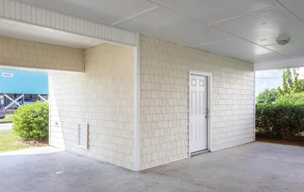 The view of a tidy white entrance door flanked by textured walls and green shrubbery, suggesting a welcoming and well-kept arrival point. The arrangement hints at a nearby parking area, inviting guests home after outings or travel.
