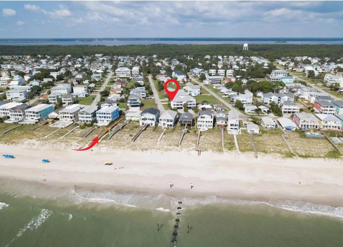 A striking view of beachfront properties with a pier stretching into clear water, sandy beaches, and the open ocean. The scene is full of potential activity—swimming, fishing, walking along the shore—while conveying the quintessential coastal experience.