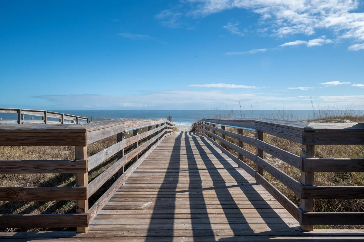 This image shows a wooden boardwalk leading out to a breathtaking ocean view, with the horizon stretching in the distance. The scene is peaceful and natural, inviting visitors to imagine themselves strolling toward the beach, scanning for wildlife or simply soaking up the coastal atmosphere.